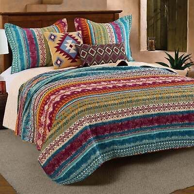 a bed with colorful bedspread and pillows on it in a room next to a potted plant