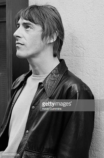 a young man wearing a leather jacket leaning against a wall