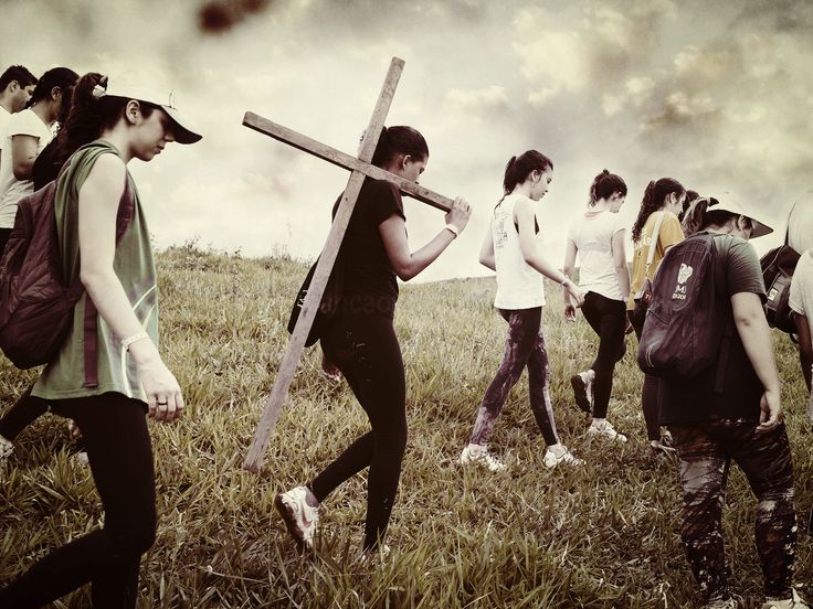 a group of people walking across a grass covered field with a cross on their back