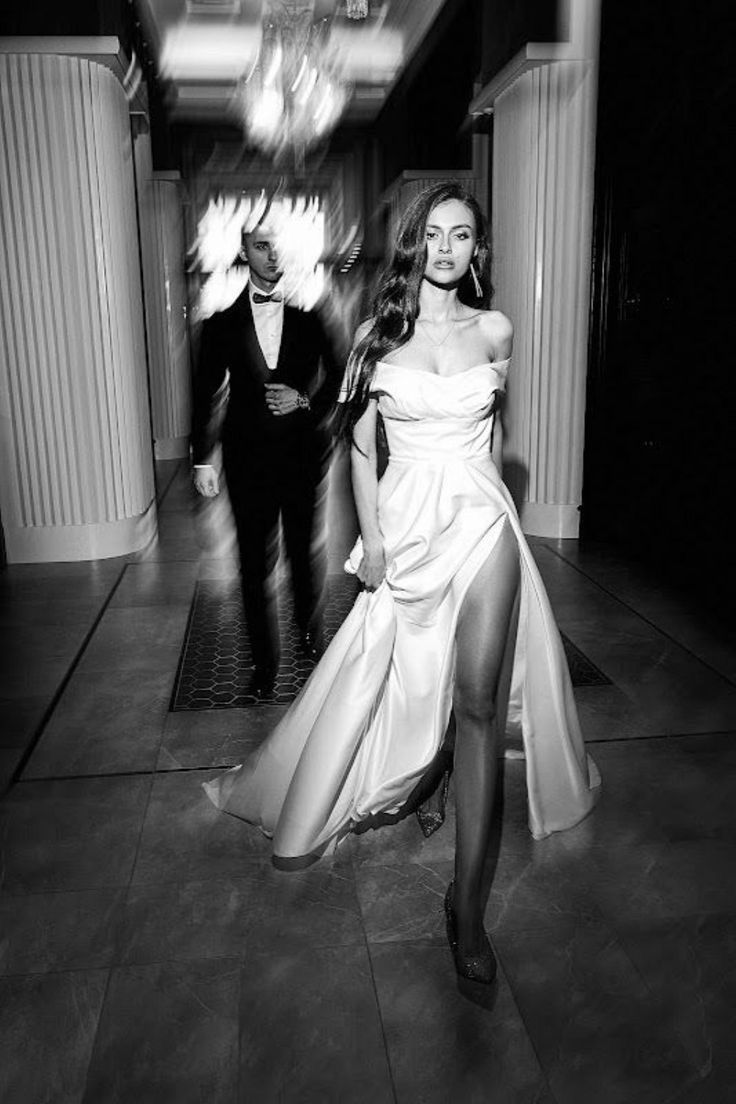 a black and white photo of a woman in a long dress walking down a hallway