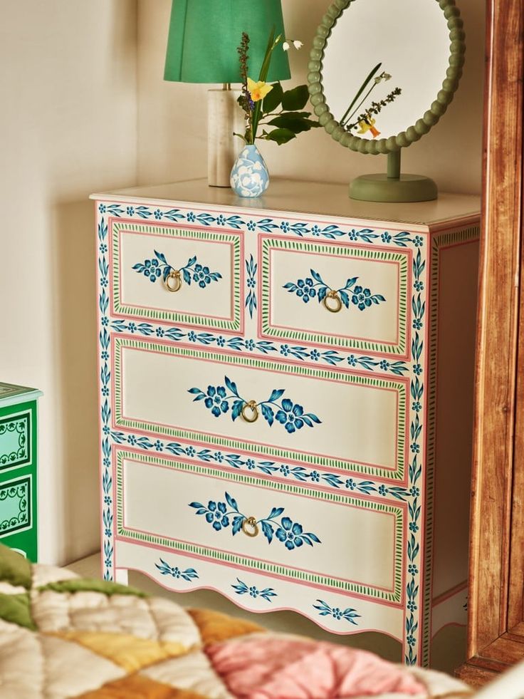 a white dresser with blue flowers on it and a green lamp next to the dresser