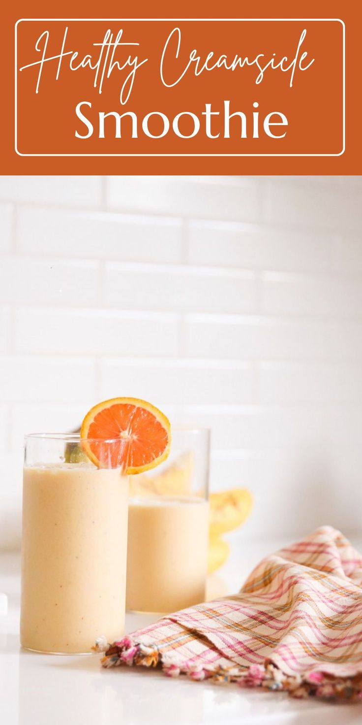 two glasses filled with smoothie sitting on top of a counter next to an orange slice