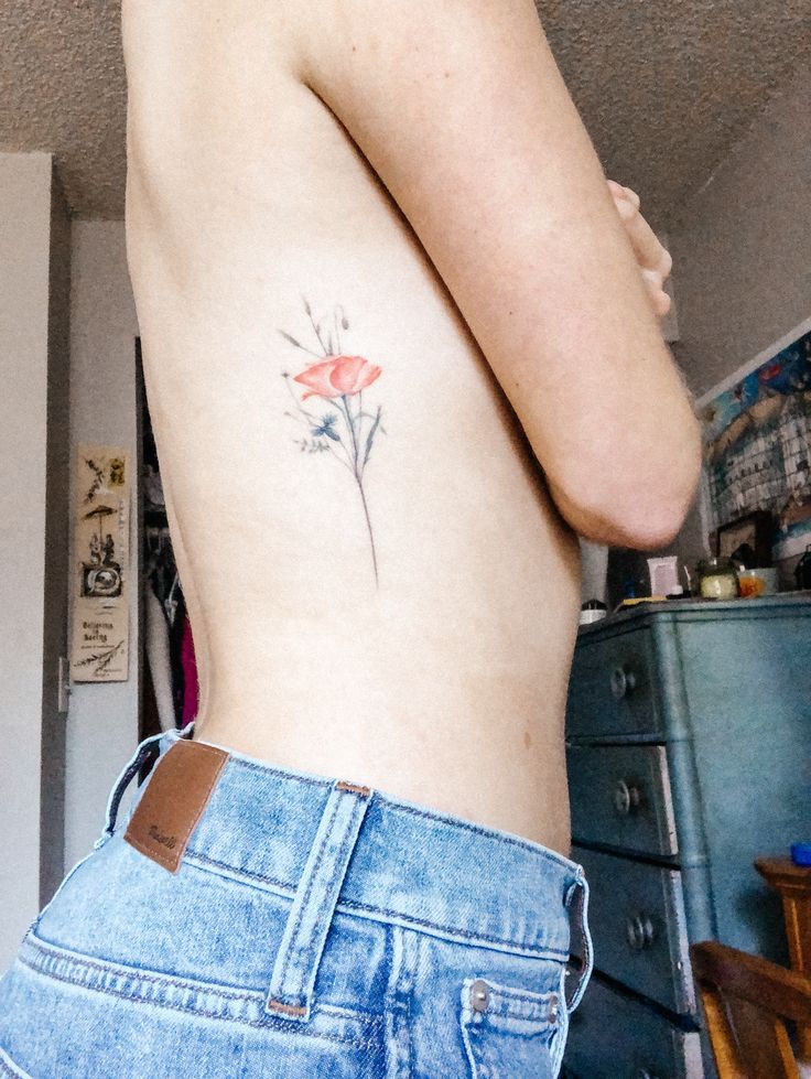 a woman with a flower tattoo on her left side ribcage is looking at the camera