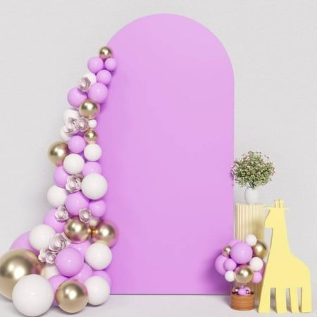 a purple and white backdrop with balloons, giraffes and a plant in the foreground