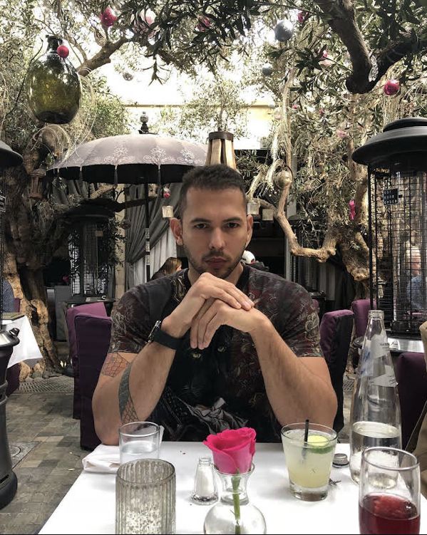 a man sitting at a table with drinks in front of him and an open birdcage behind him