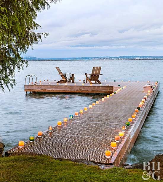 two lawn chairs sitting on top of a wooden dock next to the ocean with floating candles