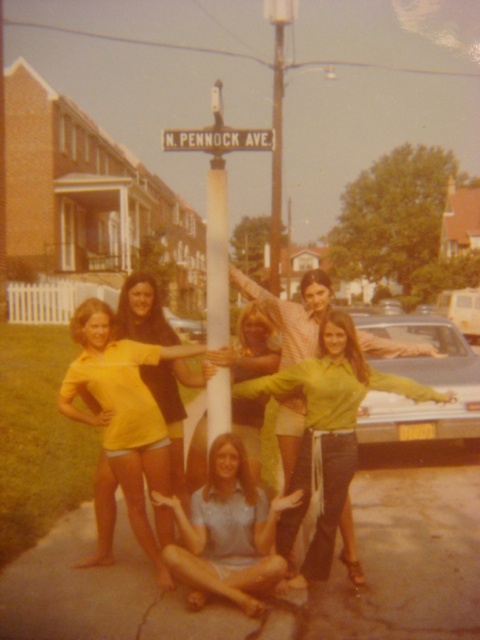 a group of young women standing next to each other on a sidewalk near a street sign