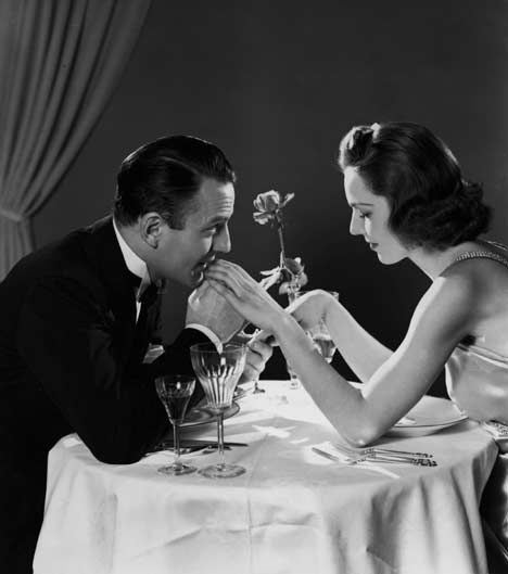 a man and woman sitting at a table with wine glasses in front of them, saying i love when we do romantic things