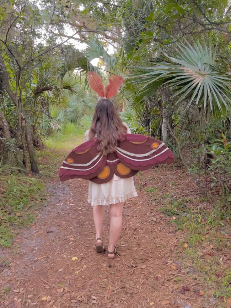 a woman walking down a dirt road with a butterfly wings on her head and back