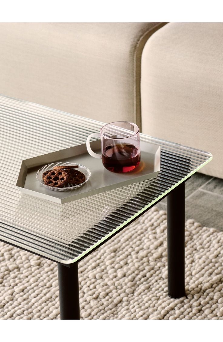 a glass table topped with a cookie and cup of coffee on top of it next to a couch