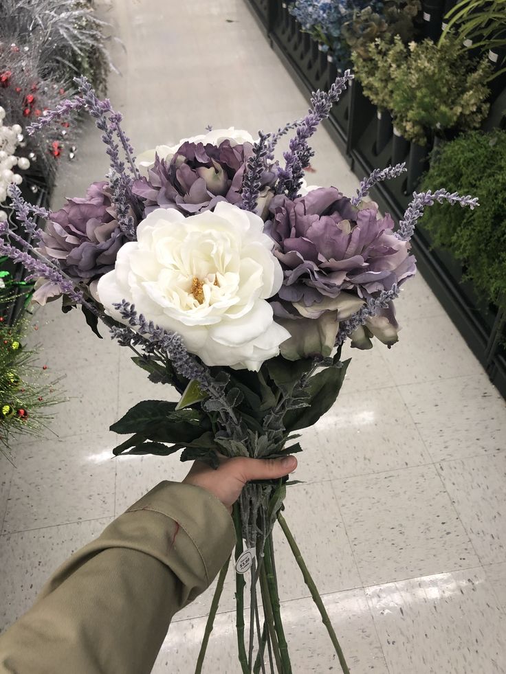 a bouquet of flowers is being held by a person in a store aisle with other plants