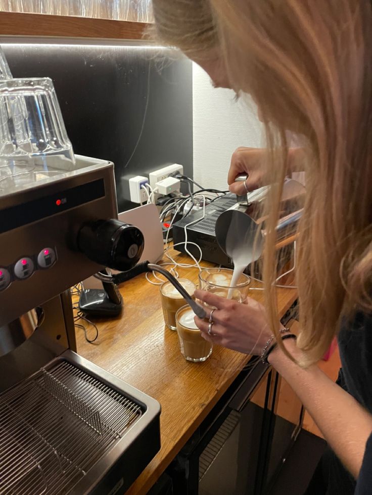 a woman pours coffee into a glass in front of an espresso machine