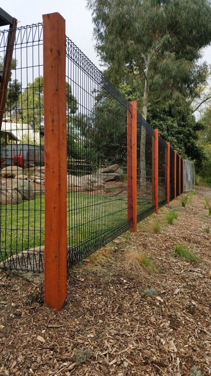 the fence is made of metal wire and has wood posts on each side, along with mulch