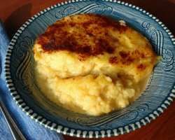 mashed potatoes in a blue bowl on top of a wooden table next to a fork