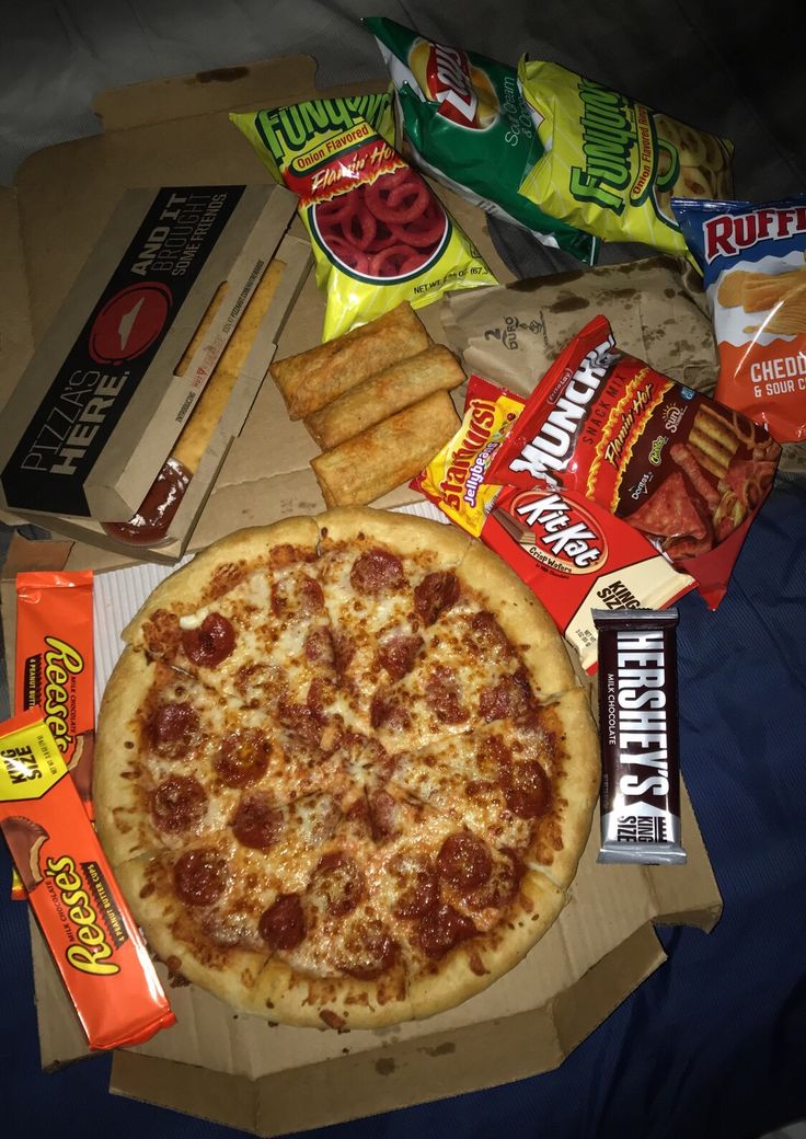 a pizza, chips and snacks on a bed