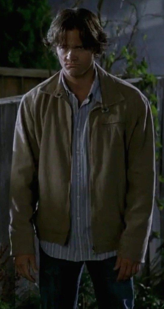 the young man is wearing a jacket and standing in front of an outdoor area at night