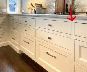 a kitchen with white cabinets and wood flooring has an arrow pointing to the left