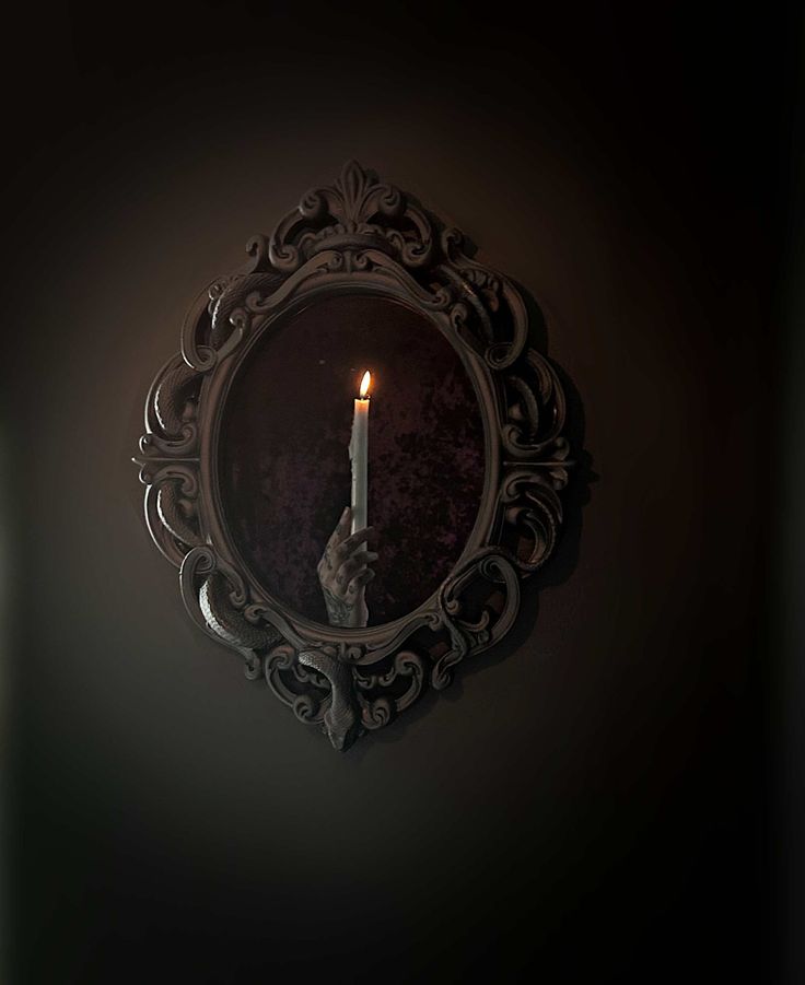 a candle is lit in front of a mirror on the wall with black walls behind it