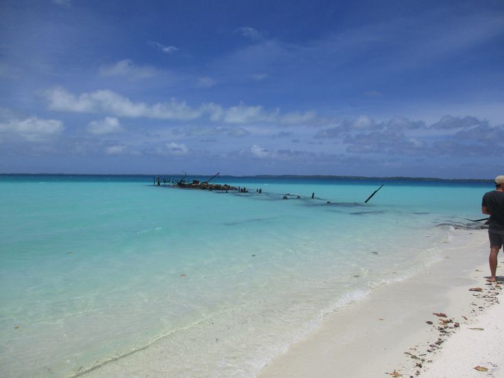 a man standing on the beach looking out at boats in the water and people walking along the shore