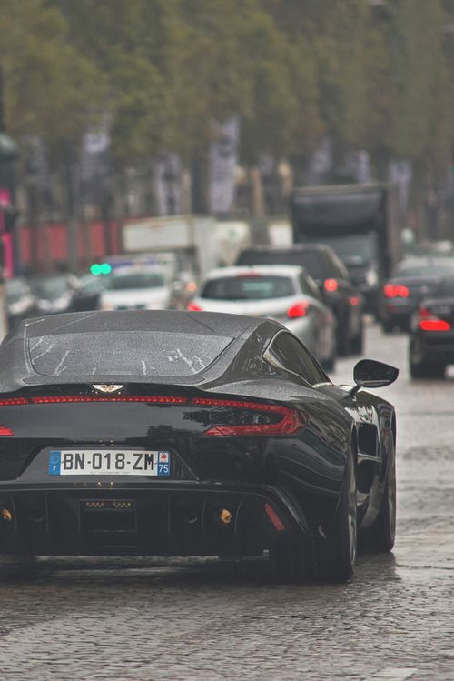 a black sports car is driving down the street in the rain with other cars behind it