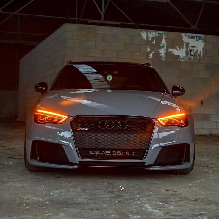 the front end of an audi car with its lights on in a parking lot at night