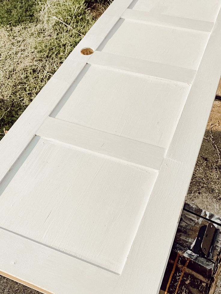 an open white door sitting on top of a wooden floor next to a building and grass