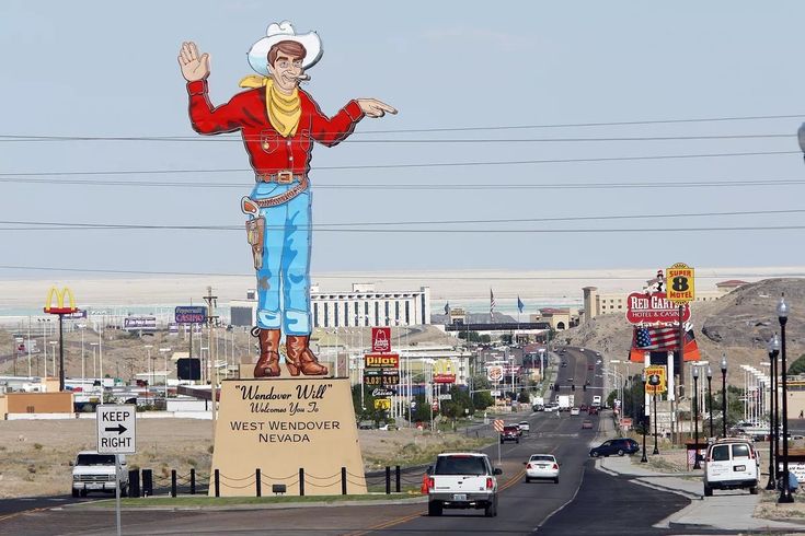 a large statue of a cowboy on top of a sign in the middle of a road