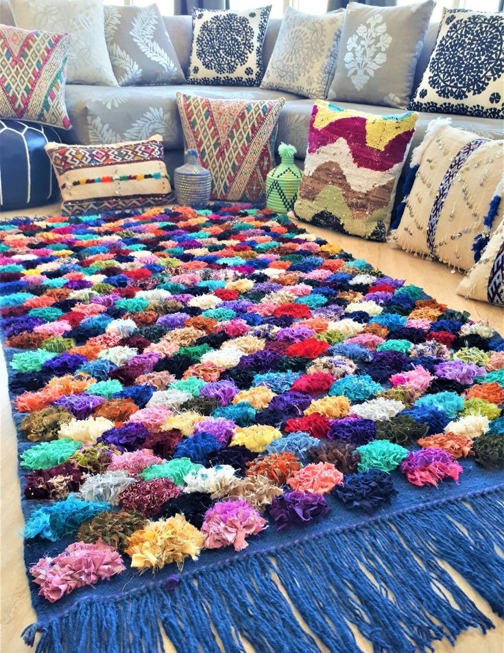 a multicolored rug on the floor in front of a couch with pillows and throw pillows