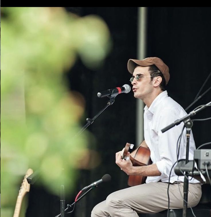 a man sitting on top of a stage while playing a guitar and singing into a microphone