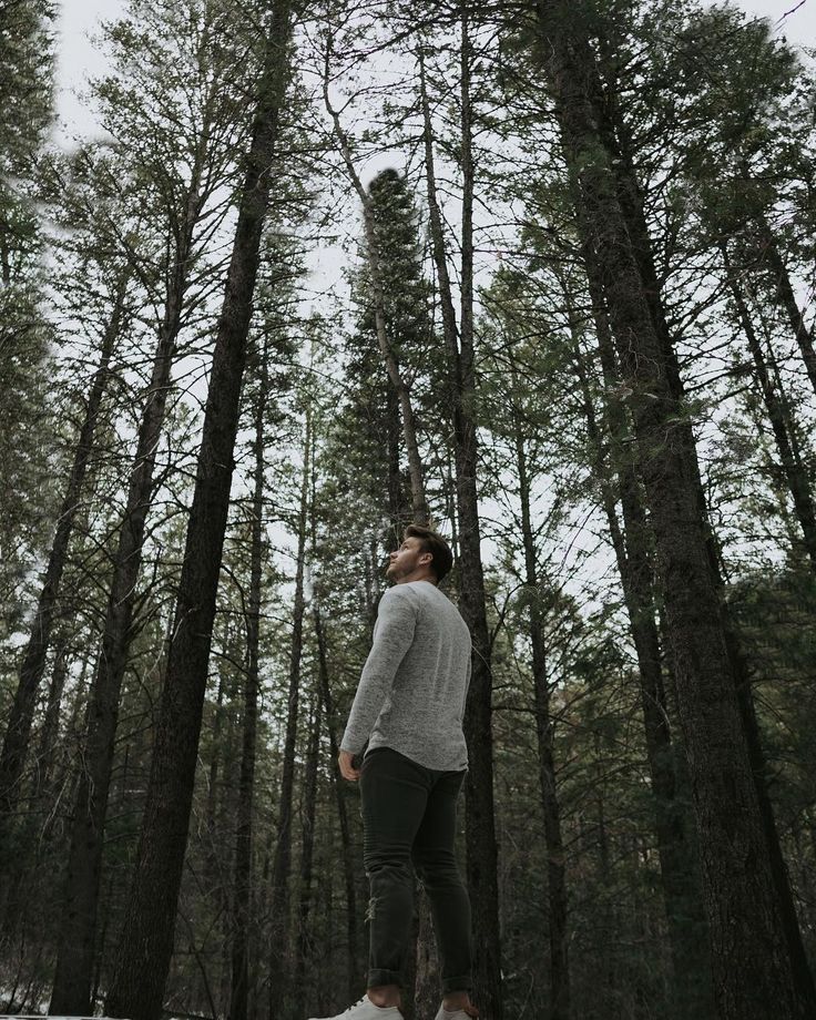 a man standing in the middle of a forest looking up into the sky with his eyes closed