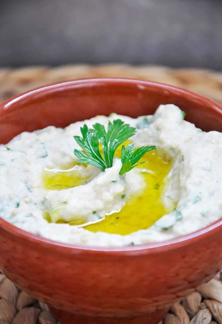 a red bowl filled with hummus and parsley on top of a woven place mat