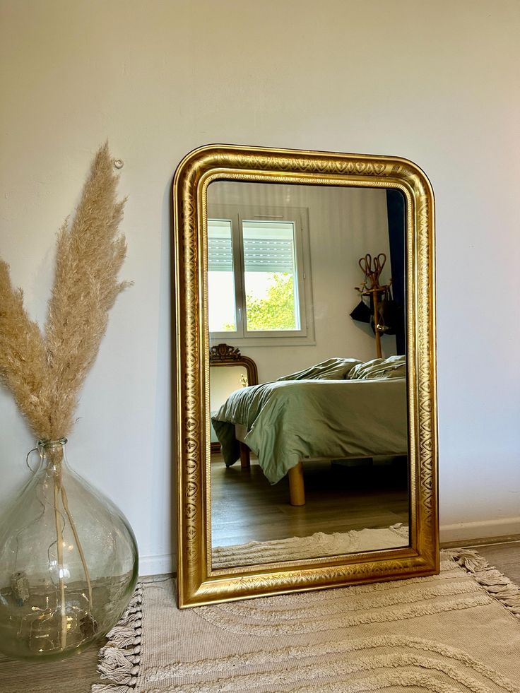 a mirror sitting on top of a wooden floor next to a vase