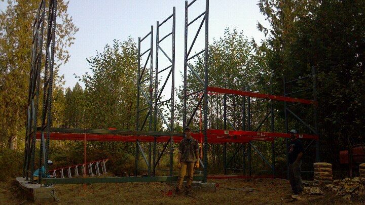 two men are working on a metal structure in the middle of a wooded area with tall trees