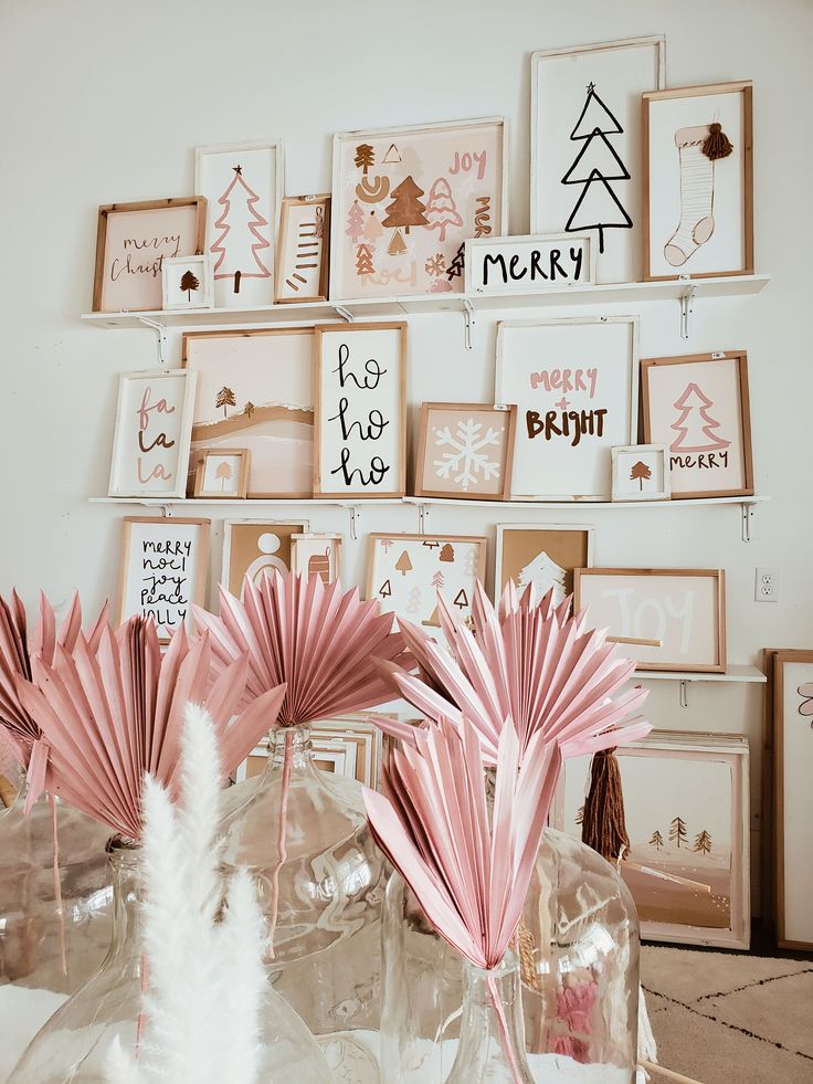 pink paper flowers are in vases on a table with pictures and framed art behind them