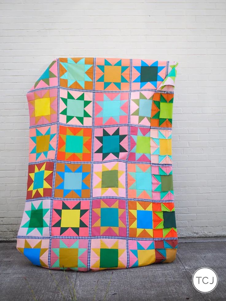 a large colorful quilt sitting on top of a cement floor next to a white brick wall