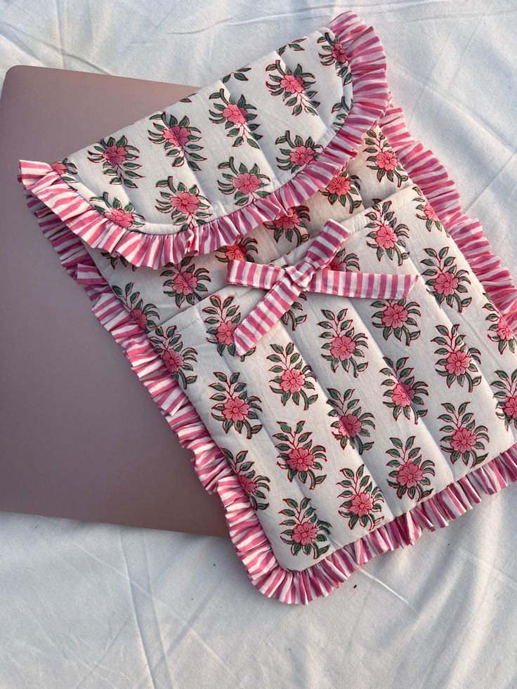 an open laptop computer sitting on top of a white bed covered in pink and green flowers