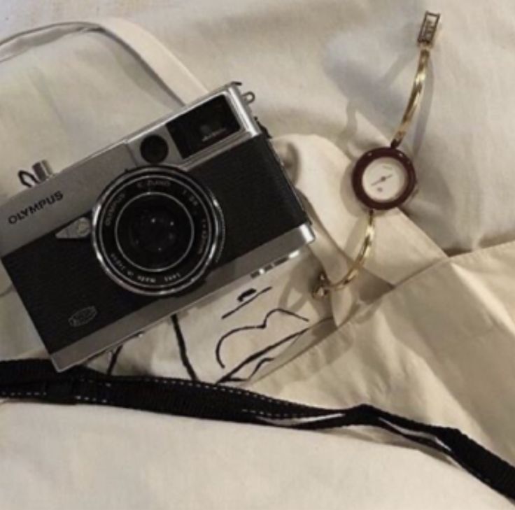 a camera sitting on top of a bed next to a white sheet and a watch