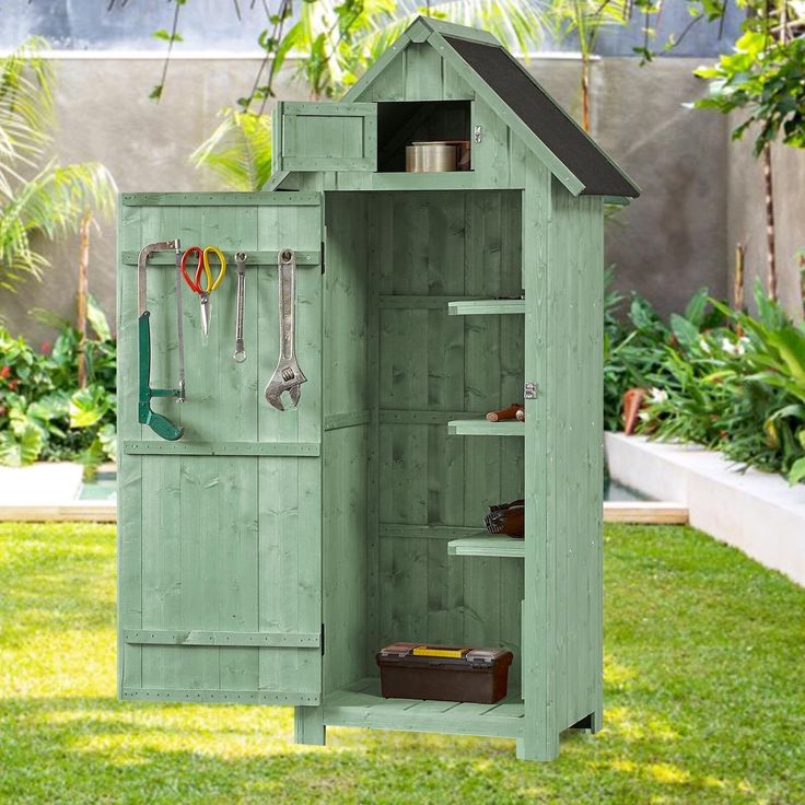 a green shed with tools hanging from the roof and shelves on it's side