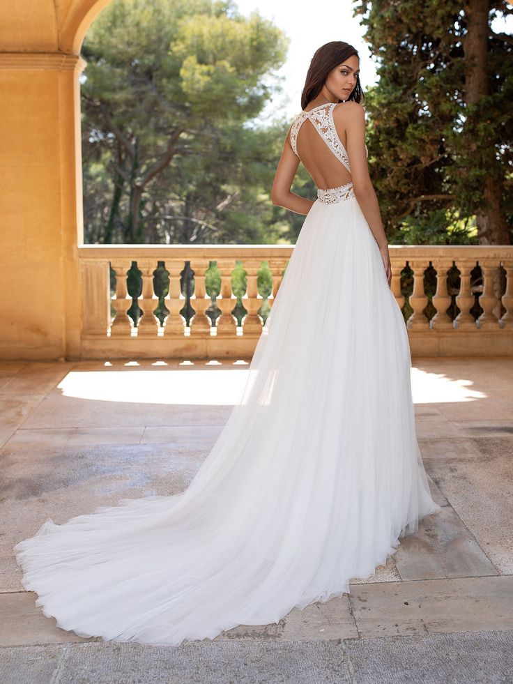 a woman in a white wedding dress standing on a balcony looking at the trees and bushes