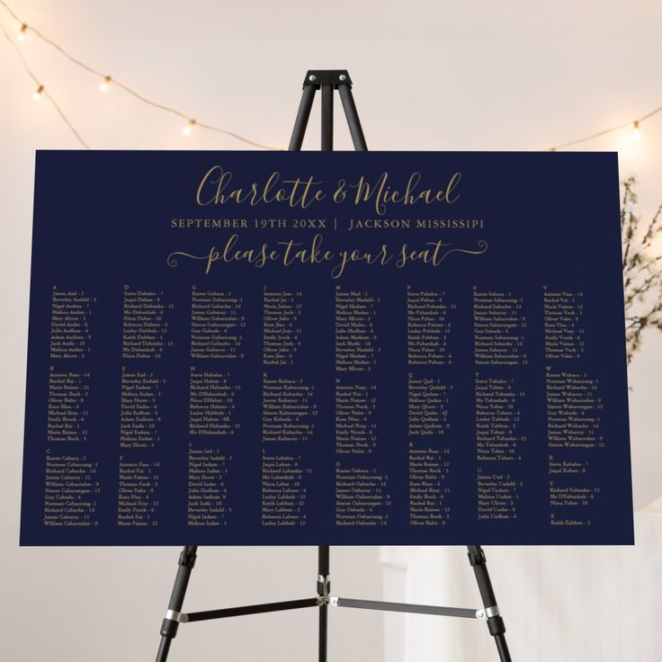 a blue and gold wedding seating chart on a easel with lights in the background