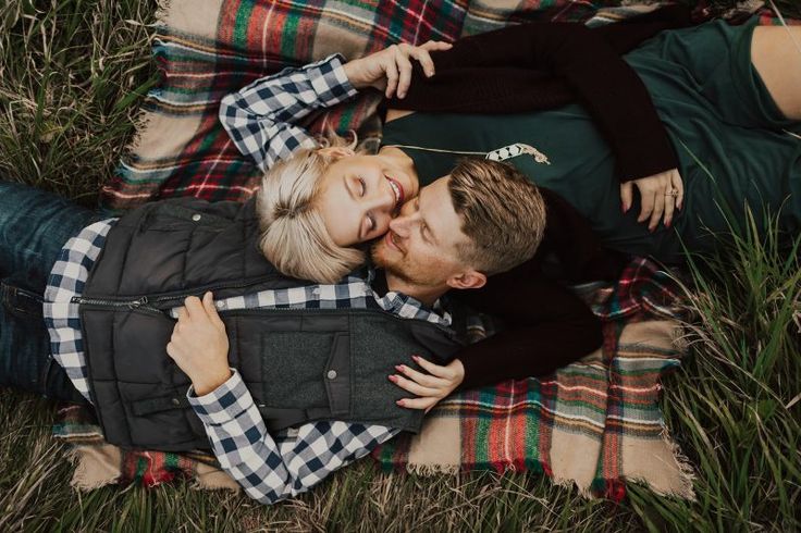 a man and woman laying on top of a blanket in the grass kissing each other