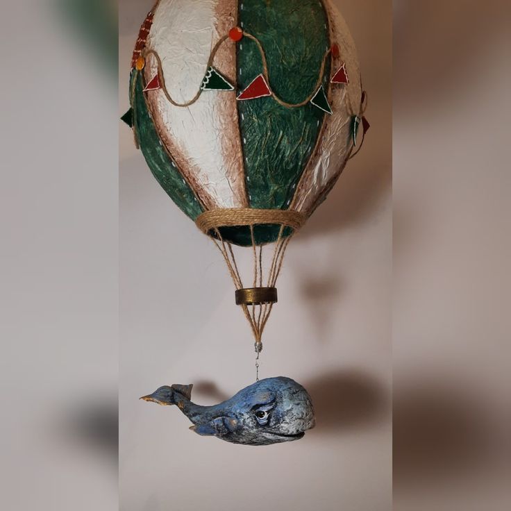 a hot air balloon with a bird hanging from it's side, and an ornament attached to the bottom