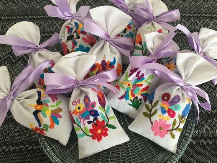 embroidered tea bags with ribbons tied around them on a wicker tablecloth basket filled with purple ribbon