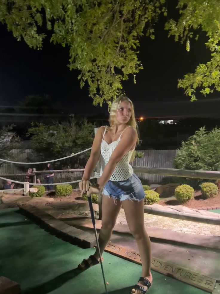 a woman is playing mini golf on the green course in front of some trees at night