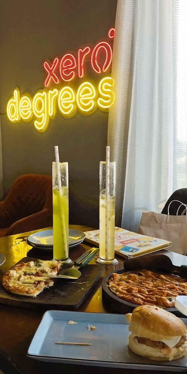 a table topped with pizza and drinks next to a neon sign that reads xero degrees