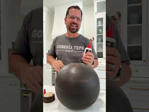 a man holding a bottle and standing next to a large metal ball in a kitchen