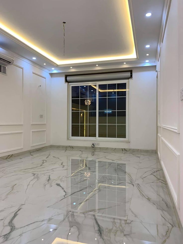 an empty room with white walls and marble flooring is lit by recessed lighting