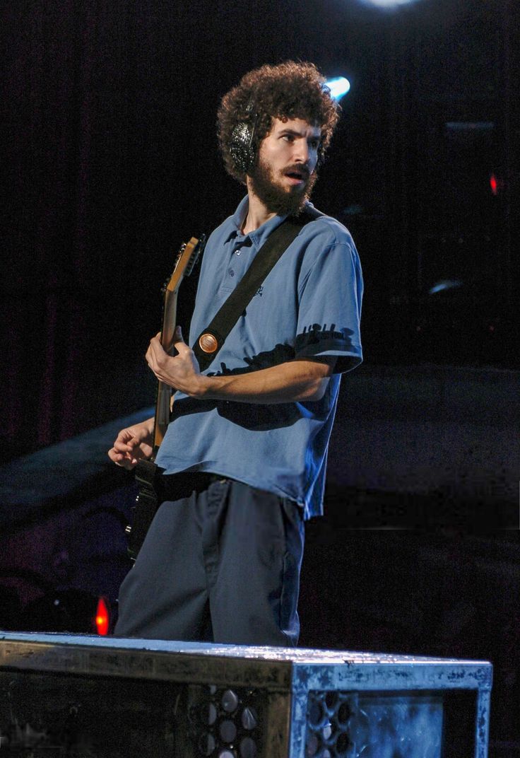 a man standing on stage with a guitar in his hand and headphones around his neck