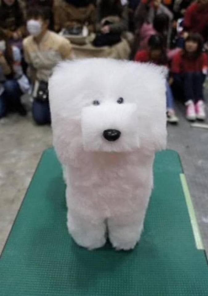 a white stuffed animal sitting on top of a green mat with people in the background