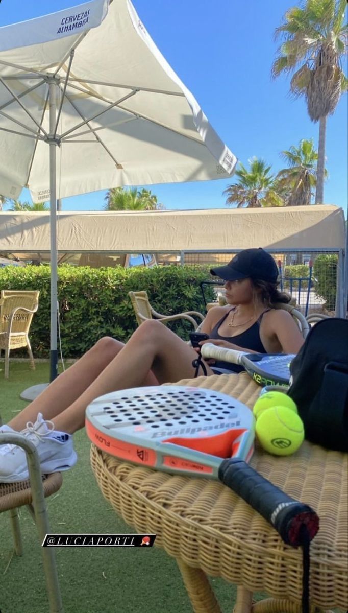 a woman sitting in a chair with tennis rackets and balls on the table next to her